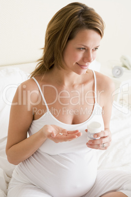 Pregnant woman in bedroom holding medicine and water smiling