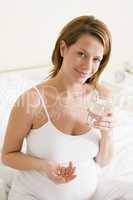 Pregnant woman in bedroom holding medicine and water smiling