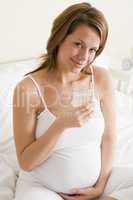 Pregnant woman sitting in bedroom with glass of water smiling