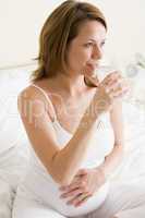 Pregnant woman sitting in bedroom with glass of water smiling