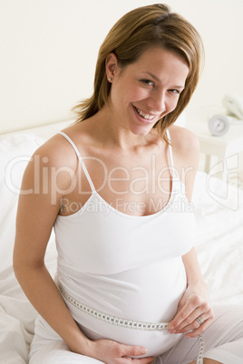 Pregnant woman in bedroom measuring belly smiling