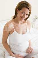 Pregnant woman in bedroom measuring belly smiling