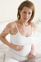 Pregnant woman in bedroom measuring belly looking worried