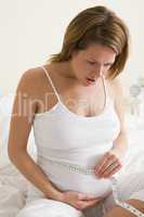 Pregnant woman in bedroom measuring belly looking worried