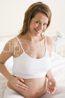 Pregnant woman in bedroom rubbing cream on belly smiling