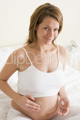 Pregnant woman in bedroom rubbing cream on belly smiling