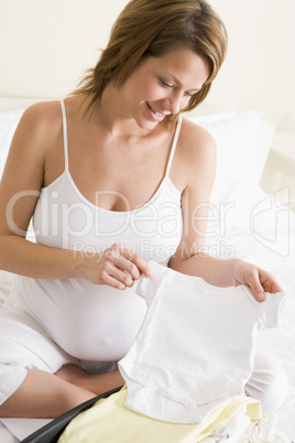 Pregnant woman packing baby clothing in suitcase smiling