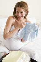 Pregnant woman packing baby clothing in suitcase smiling