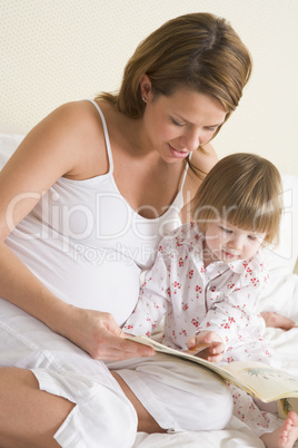 Pregnant woman in bedroom reading book with daughter