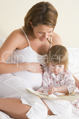 Pregnant woman in bedroom reading book with daughter