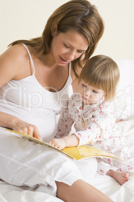 Pregnant woman in bedroom reading book with daughter