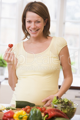 Pregnant woman in kitchen making a salad smiling