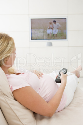 Pregnant woman watching television using remote control