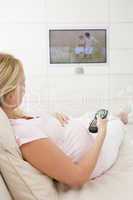 Pregnant woman watching television using remote control