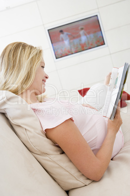 Pregnant woman reading magazine with television in background sm