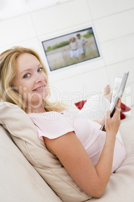 Pregnant woman reading magazine with television in background sm