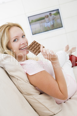 Pregnant woman watching television and eating chocolate smiling