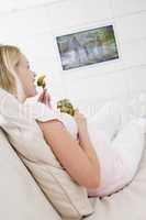 Pregnant woman watching television and eating pickles smiling