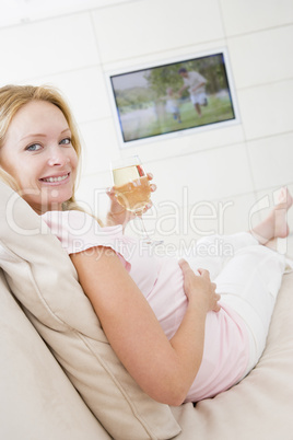 Pregnant woman watching television with glass of white wine smil