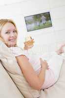 Pregnant woman watching television with glass of white wine smil