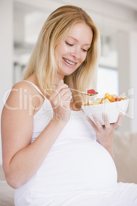 Pregnant woman with bowl of fruit salad smiling