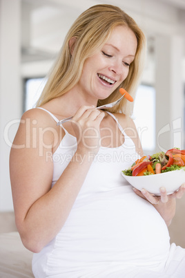 Pregnant woman with bowl of salad smiling