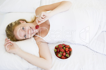 Pregnant woman lying in bed with bowl of strawberries smiling