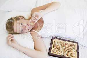 Pregnant woman lying in bed with chocolates smiling