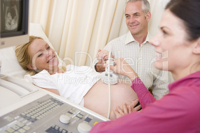 Pregnant woman getting ultrasound from doctor with husband watch