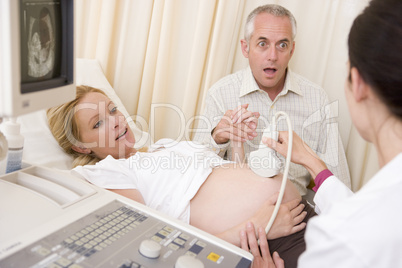 Pregnant woman getting ultrasound from doctor with husband watch