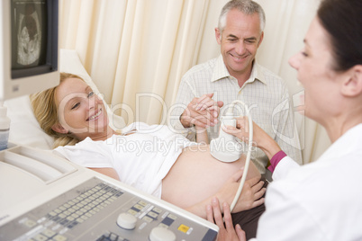 Pregnant woman getting ultrasound from doctor with husband watch