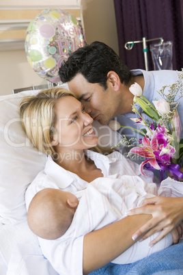 New mother with baby and husband in hospital smiling