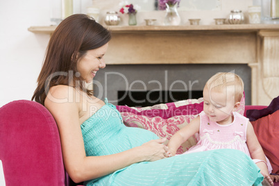 Pregnant mother with daughter in living room touching belly and