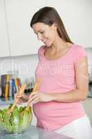 Pregnant woman in kitchen making a salad and smiling