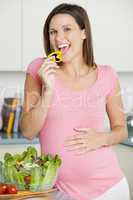 Pregnant woman in kitchen making a salad and smiling