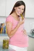 Pregnant woman in kitchen eating pickles and smiling