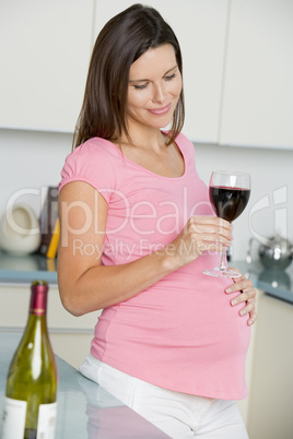 Pregnant woman in kitchen with glass of red wine smiling