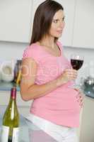Pregnant woman in kitchen with glass of red wine