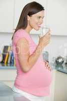 Pregnant woman in kitchen with glass of water smiling