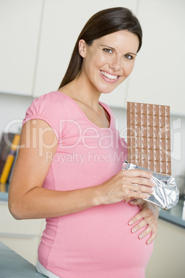 Pregnant woman in kitchen with large chocolate bar smiling