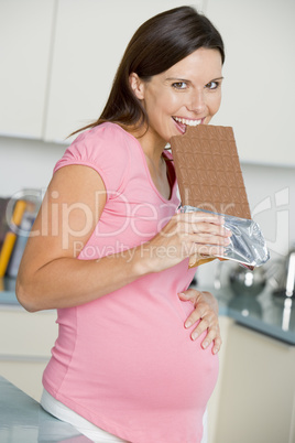 Pregnant woman in kitchen with large chocolate bar smiling