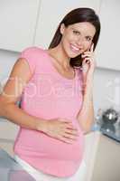 Pregnant woman in kitchen talking on cellular phone and smiling