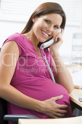 Pregnant woman at work using telephone smiling