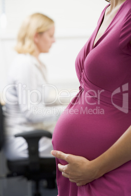 Pregnant woman at work holding belly with coworker in background