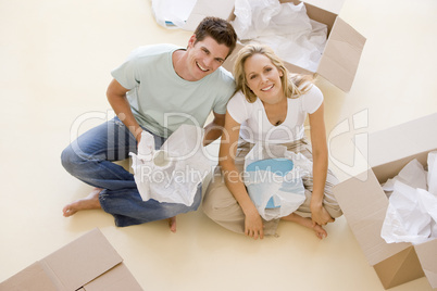 Couple sitting on floor by open boxes in new home smiling