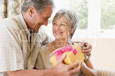 Husband giving wife gift in living room smiling