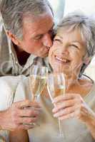 Couple in living room toasting champagne kissing and smiling
