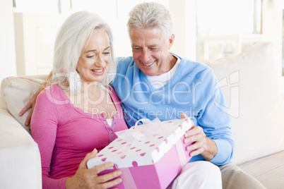 Husband giving wife gift in living room smiling