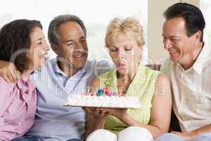 Two couples in living room smiling with woman blowing out candle