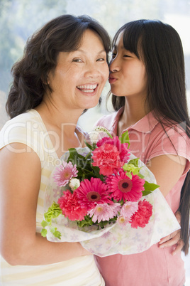 Granddaughter kissing grandmother on cheek holding flowers and s